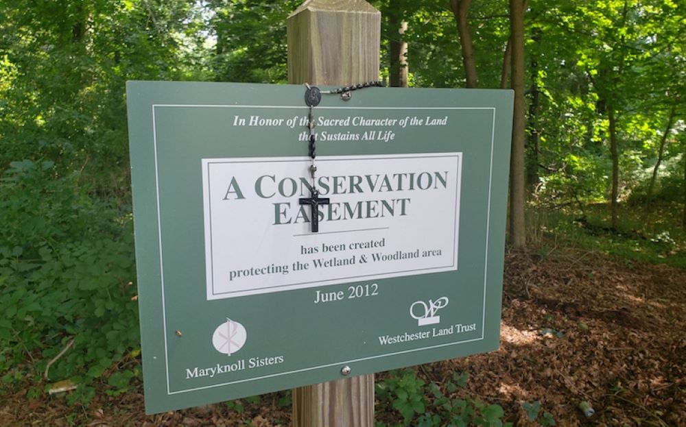 A rosary is draped over a sign marking a conservation easement on the property of the Maryknoll Sisters in Ossining, New York. (NCR photo/Chris Herlinger)