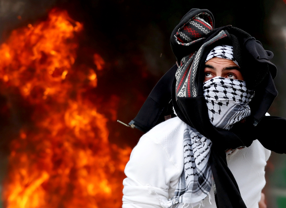 A Palestinian throws a stone at Israeli forces near Ramallah, West Bank, during a Dec. 20 protest against U.S. President Donald Trump's decision to recognize Jerusalem as the capital of Israel. (CNS/Reuters/Goran Tomasevic)