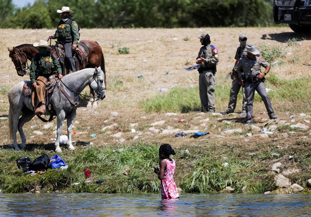 U.S. law enforcement officers in Del Rio, Texas, stand near a young migrant woman bathing in the Rio Grande Sept. 19. (CNS/Reuters/Daniel Becerril)