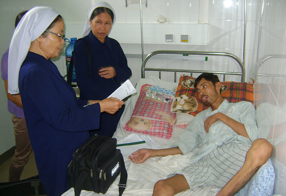 Daughters of Our Lady of the Visitation Sr. Mary Le Thi Bich (center) offers milk and money to Le Huu Tong at the Central Hospital in Hue, Vietnam, on Aug. 6, and Daughter of Our Lady of the Visitation Sr. Anna Le Thi Hue reads a benefactor's letter to him. (GSR photo/Joachim Pham)