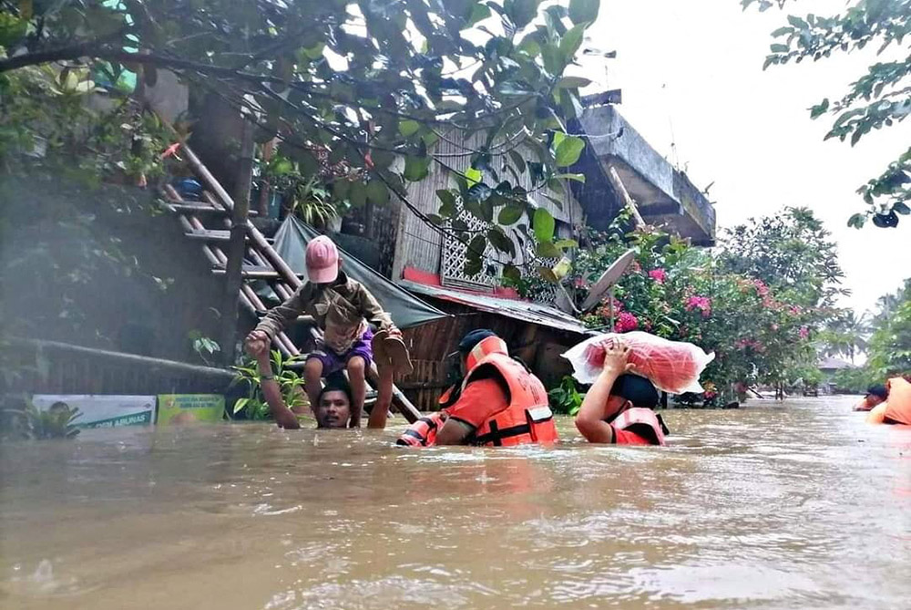 A man carries a boy on his shoulder April 10 as they walk on a flooded road after Tropical Storm Megi hit Capiz, Philippines. (CNS/Philippine Coast Guard Handout via Reuters)