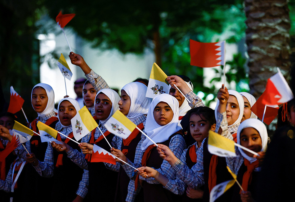 Young people wave flags of the Vatican and Bahrain as they wait for Pope Francis Nov. 3 outside the Sakhir Royal Palace. The pontiff is on a four-day visit to Bahrain. (CNS/Reuters/Yara Nardi)