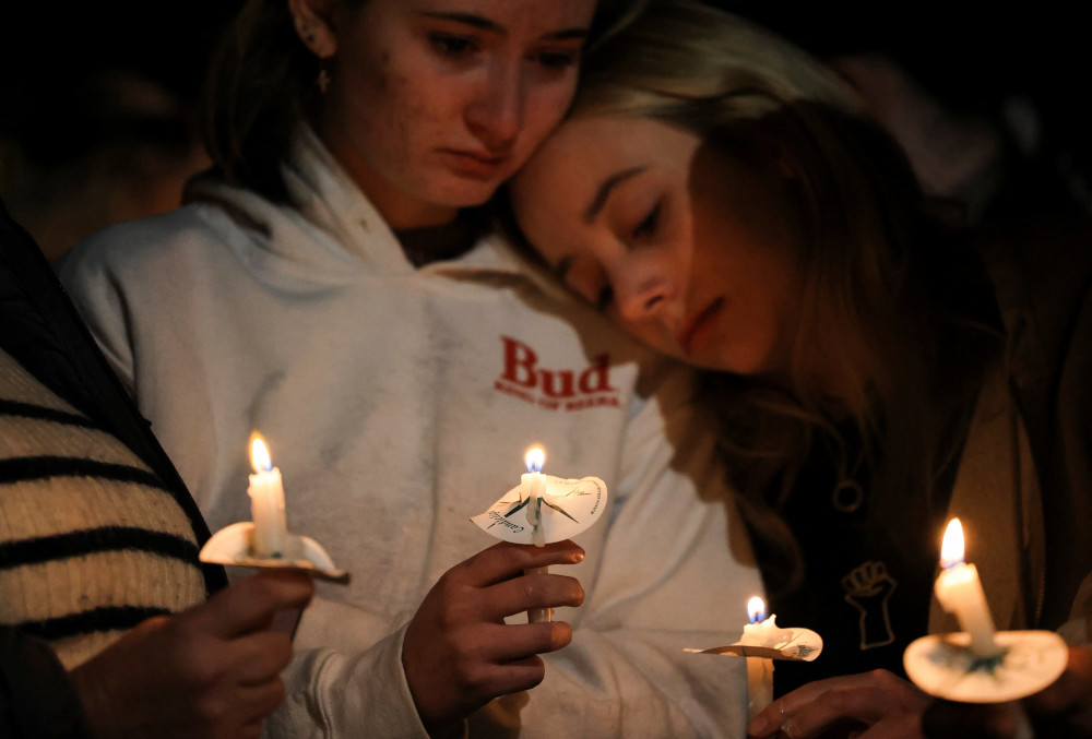 One person leans on another as they hold candles