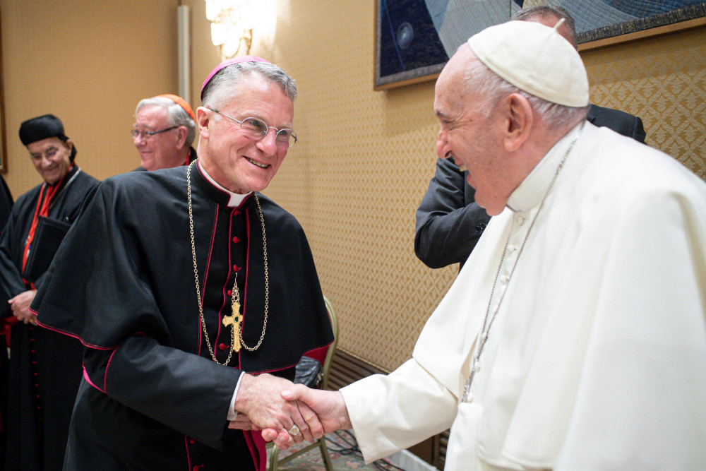 Archbishop Timothy Broglio and Pope Francis shake hands and smile at each other