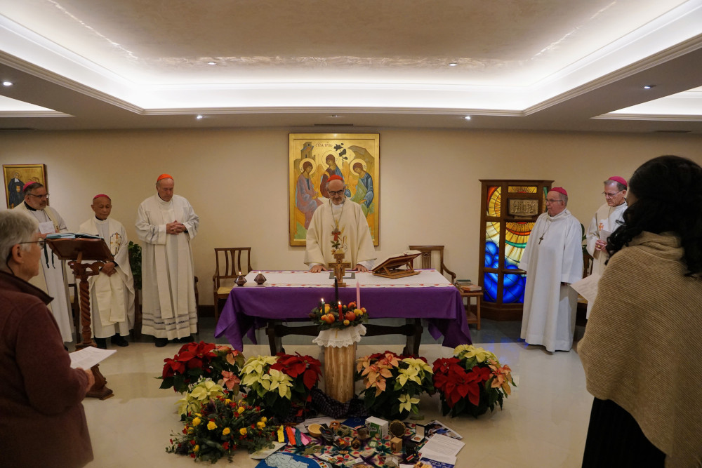 Cardinals and bishops stand behind a purple altar and poinsettia flowers to celebrate mass