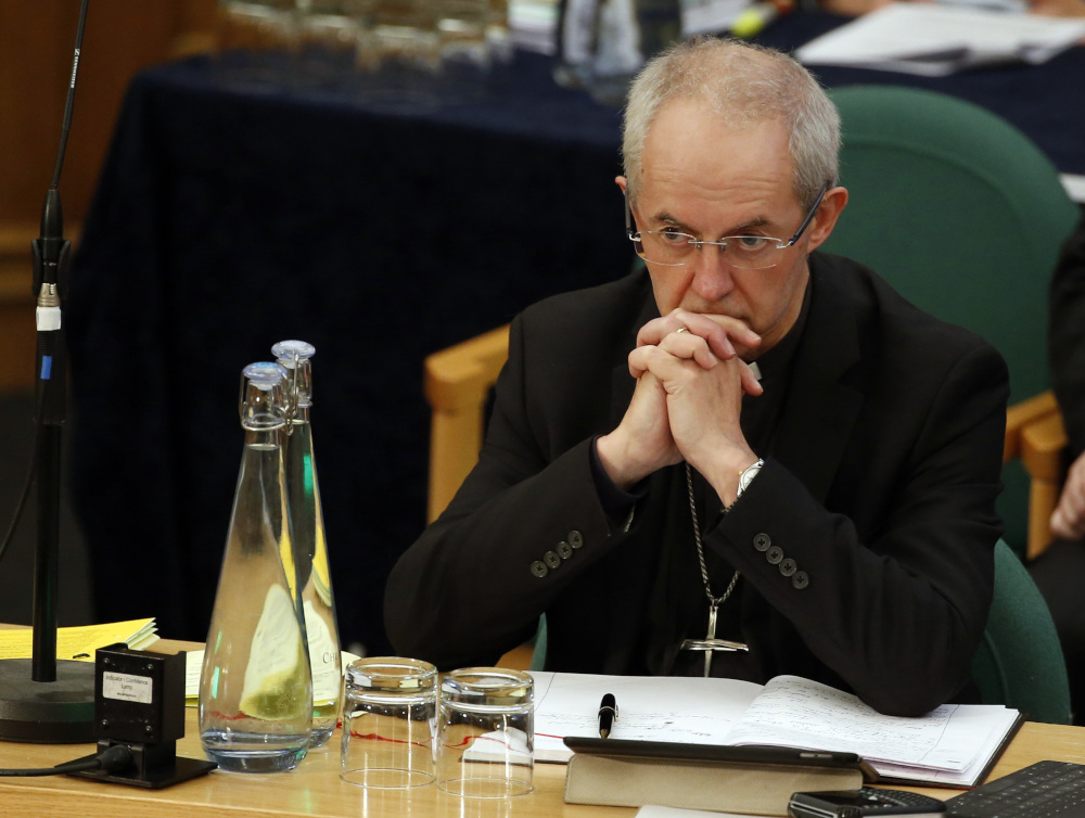 Justin Welby sits in a chair at a table with his hands folded in front of his face