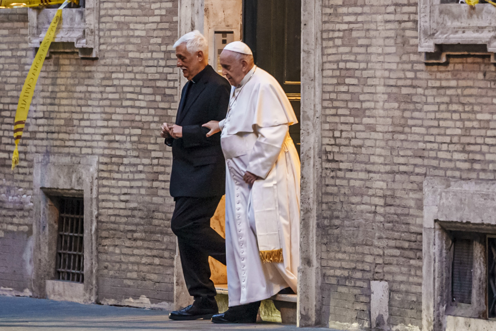 Pope Francis and a priest leave a brick building together