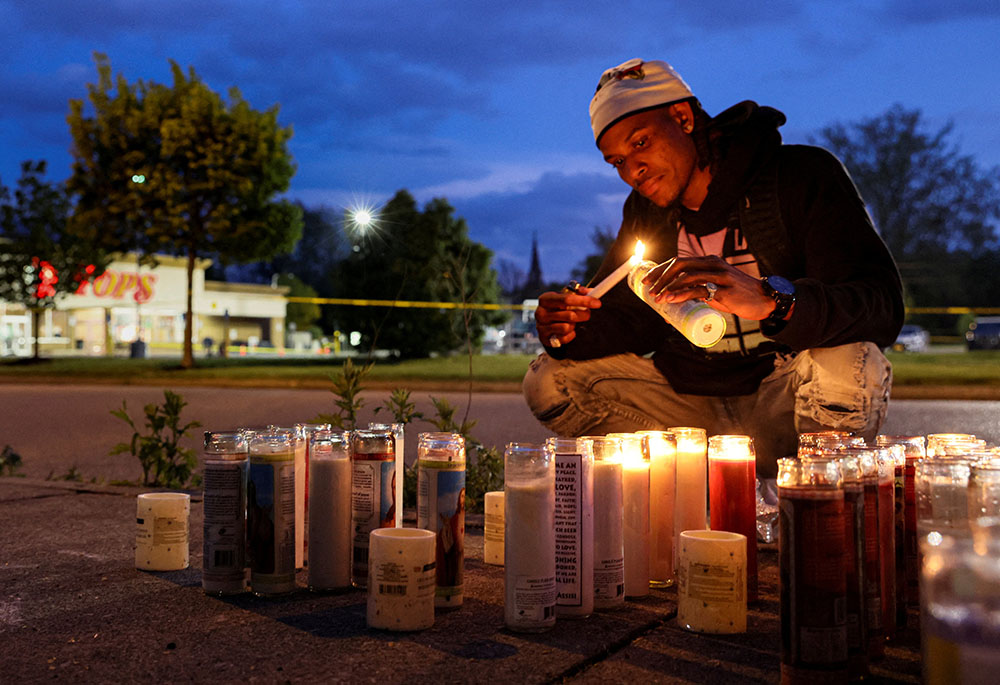 A man at a Tops supermarket in Buffalo, New York, lights a candle May 16 for the victims of a May 14 mass shooting that authorities said was motivated by racism. (CNS/Reuters/Brendan McDermid)