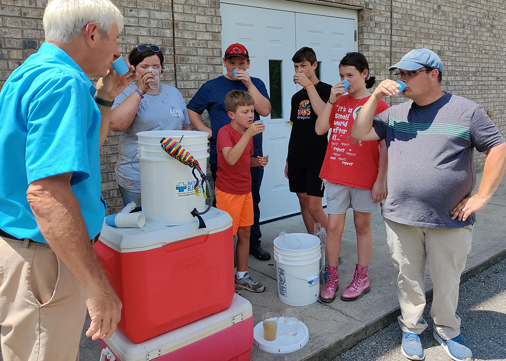 Arnie LeMay of Water With Blessings, left, drinks a cup of filtered creek water Aug. 9 in Chavies, Kentucky, after demonstrating the Sawyer PointONE water filter to volunteers at First Church of God. (CNS/Handout via The Record)