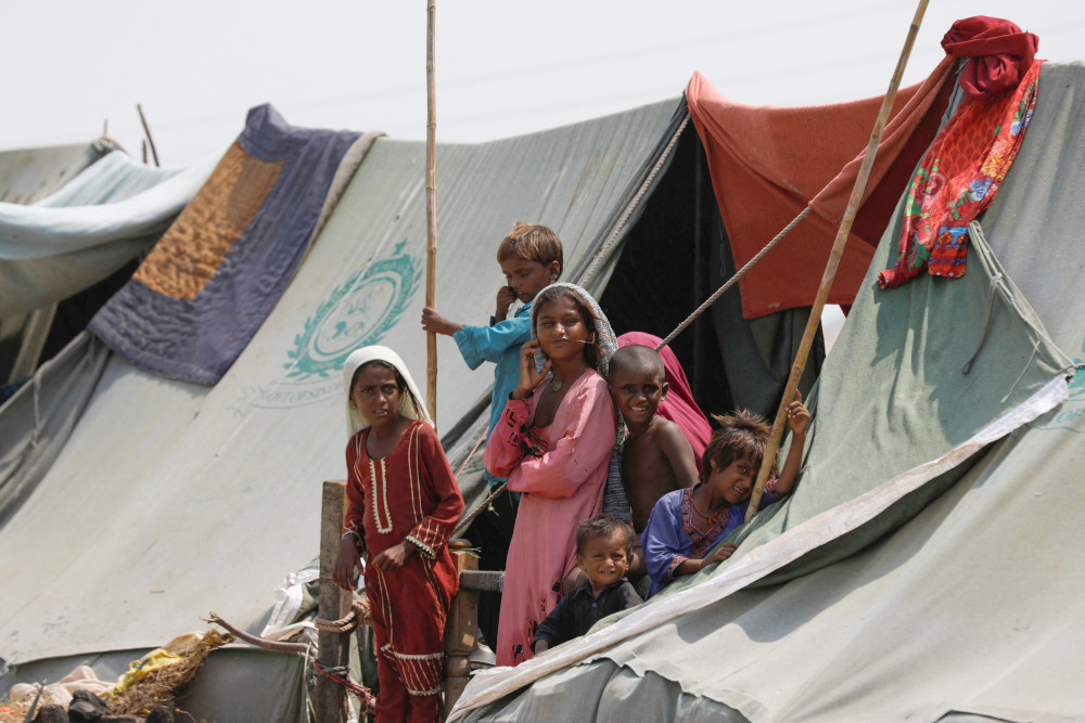 Children displaced by flooding stand outside their family tent while waiting for food handouts and relief material in Sehwan, Pakistan