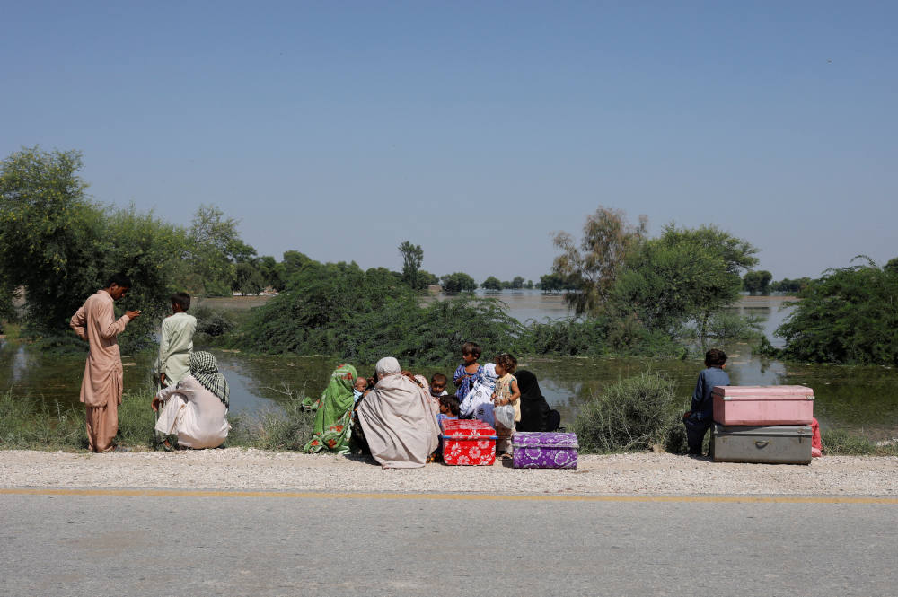 A displaced family sits with their belongings along a road with rising flood water, following rains and floods during the monsoon season in Bhan Syedabad, Pakistan, Sept. 8, 2022. (CNS photo/Akhtar Soomro, Reuters)