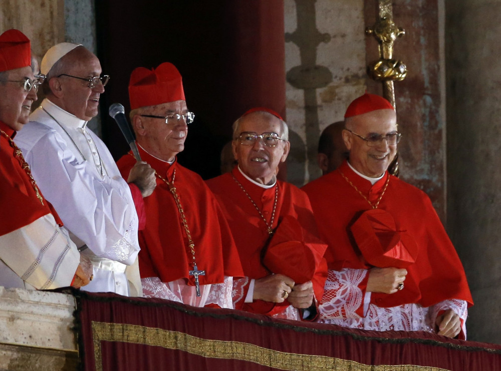 Pope Francis, wearing papal white, stands among four cardinals wearing birettas and zucchettos on a balcony