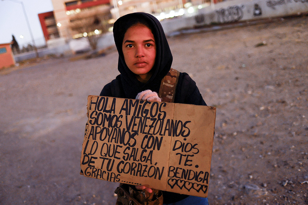 Yalimar Chirinos, a 19-year-old migrant from Venezuela, displays a sign near the U.S.-Mexico border in Ciudad Juárez, Mexico, Jan. 7. The sign reads, "Hello friends, we are from Venezuela, support us with what comes out from your heart. Thank you. God bless you." (OSV News/Reuters/Jose Luis Gonzalez)