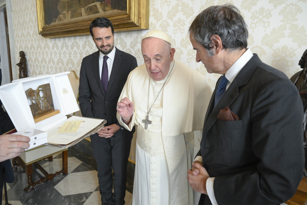 Pope Francis closes his fingertips in a hand gesture as he speaks to an older white man in a suit