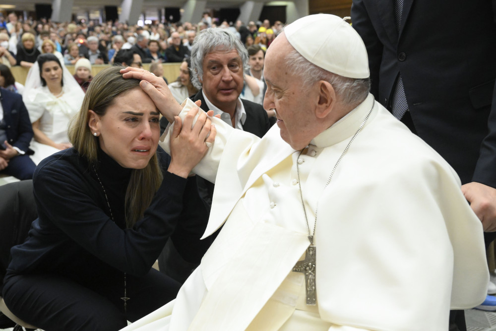 Pope Francis places his hand on the head of a woman who cries with emotion