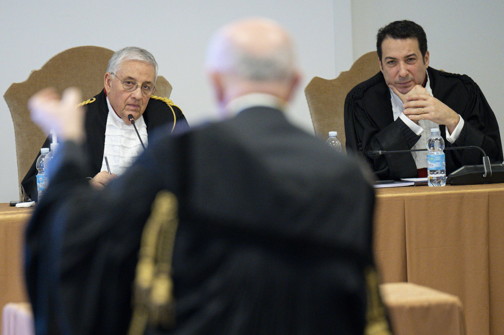 Two men in black jackets and frilly white shirts listen to another man in a suit