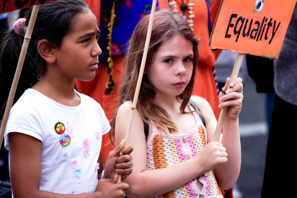 Two young girls stand side by side. One holds a sign that says "Equality."