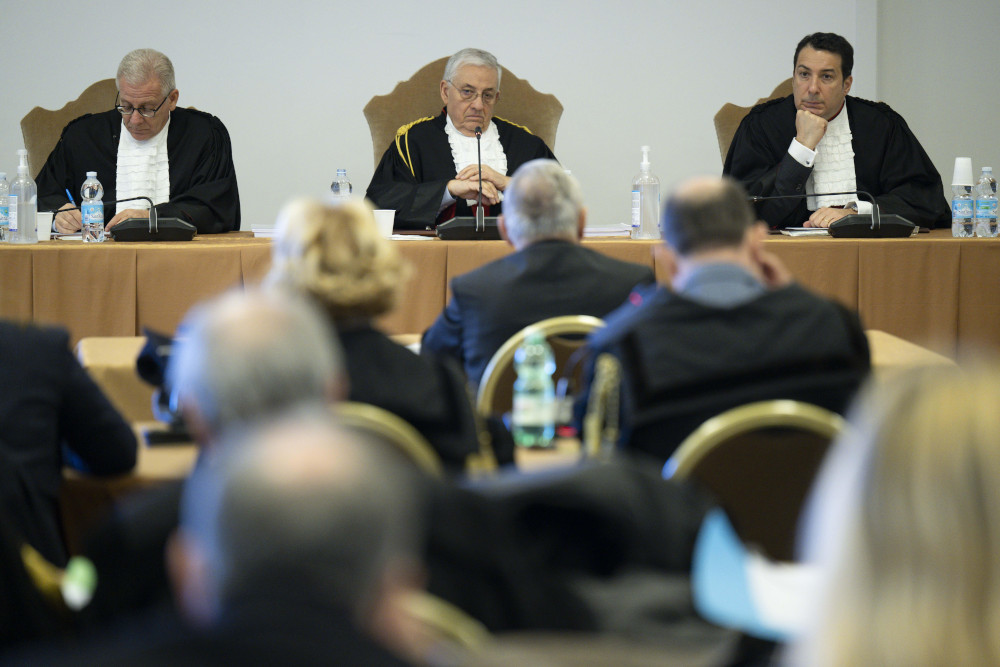 Three white men sit above a larger room wearing white ruffled shirts and black jackets