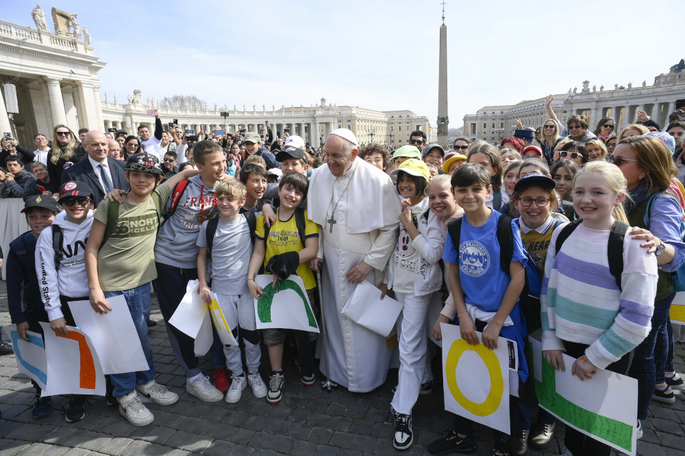 Pope Francis stands among a group of children who look elementary-school-aged in St. Peter's Square