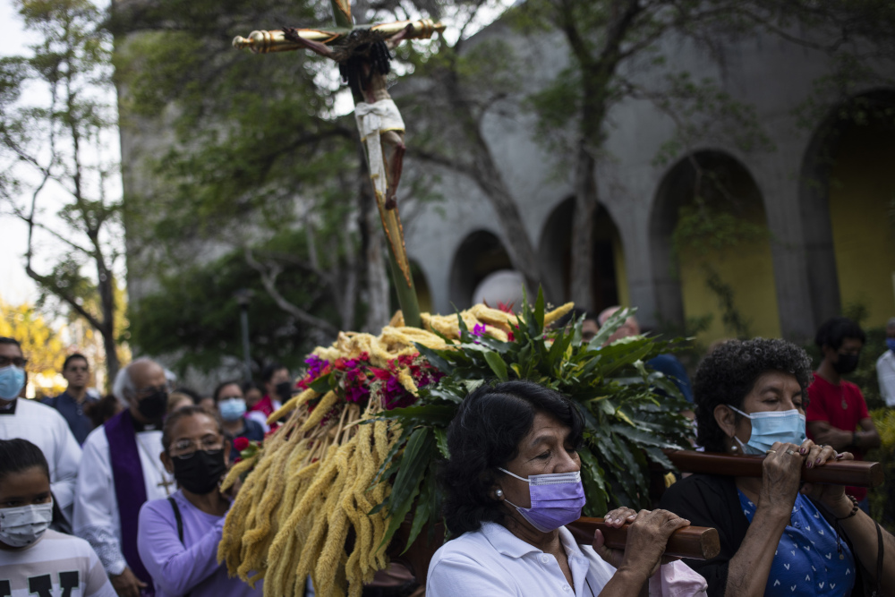 Three masked women can be seen carrying a crucifix on their shoulders surrounded by a larger masked crowd