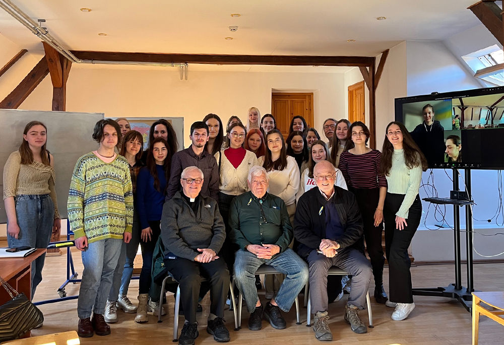 A class of sociology and social work majors is pictured at the Ukrainian Catholic University in Lviv. Seated in front is NCR contributor Fr. Peter Daly; Jim McDermott; and NCR board member David Bonior, who were visiting Ukraine and Poland. Professor Bob Wood is fourth from the right, back row. The monitor on the right shows a student in fatigues who is a medic with her unit in Bakhmut. (Courtesy of David Bonior)