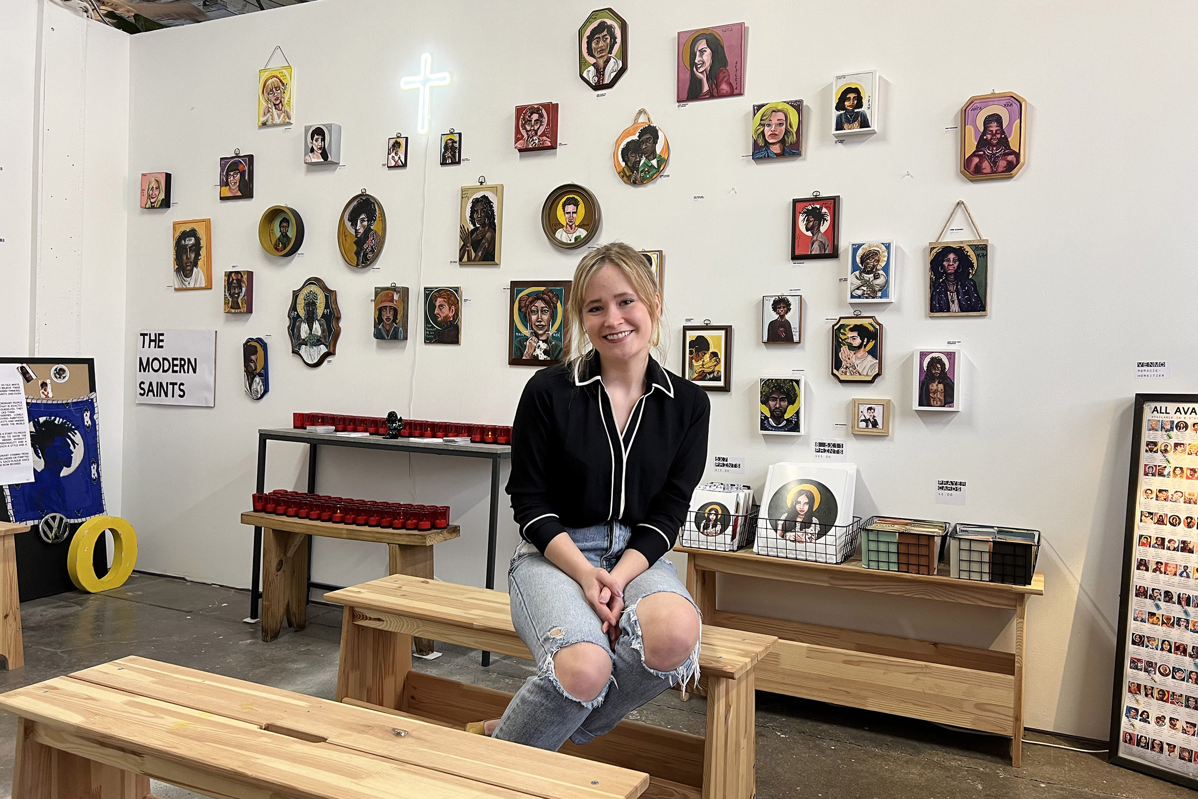 Gracie Morbitzer, a young white woman in ripped jeans and a black top, sits on a bench in her studio