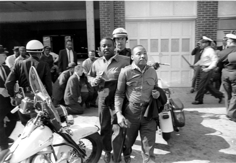 Martin Luther King and another Black man stand in front of a white police officer with a scooter