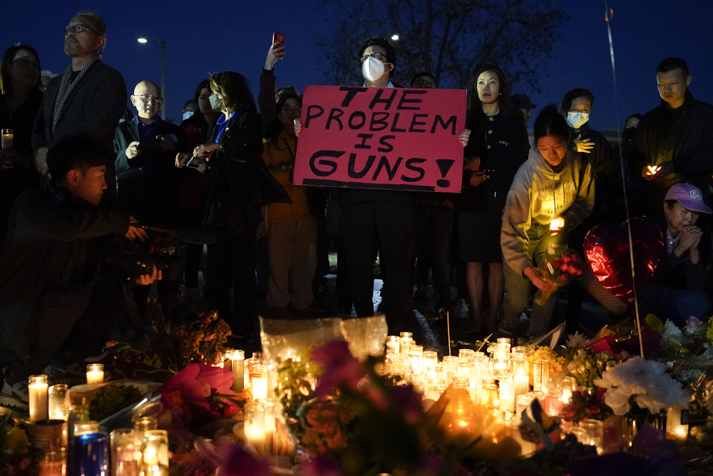 A man holds a sign during a vigil outside Monterey Park City Hall, blocks from the Star Ballroom Dance Studio, Jan. 24, in Monterey Park, California. (AP/Ashley Landis)