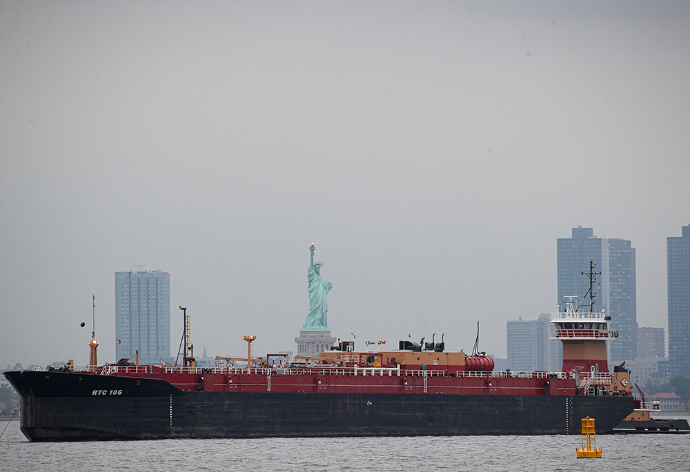  A tugboat in New York City pushes a fuel oil barge past the Statue of Liberty Oct 13, 2021. (CNS/Reuters/Brendan McDermid)