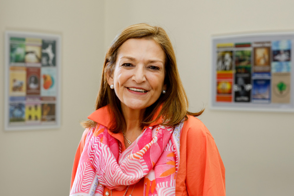 A woman with light brown hair and wearing a pink and orange scarf and orange shirt smiles into the camera