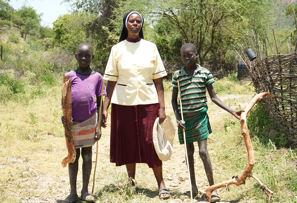 Incarnate Word Sr. Jannifer Hiuhu, a community leader at the Rotu Mission, welcomes two children bearing firewood as gifts at her congregation's mission center. The firewood will be used to cook porridge, which is provided daily to all children in the village as part of the sisters' effort to combat hunger and improve nutrition among the most vulnerable in rural East Pokot. (GSR photo/Wycliff Peter Oundo)