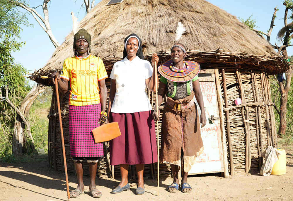 Sr. Jannifer Hiuhu with Cheposolowitch Akoler and her husband in front of their hut, clad in traditional ceremonial regalia. Despite being nomadic, Akoler's family has settled in Rotu village due to the providence of the Incarnate Word Sisters in their mission to combat hunger and elevate the living standards in the community. She fled her former village in West Pokot after it was devastated by drought. (GSR photo/Wycliff Peter Oundo)