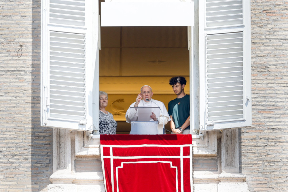 Pope Francis stands in his apartment window with an older white woman to his left and a white young man with brown hair to his right