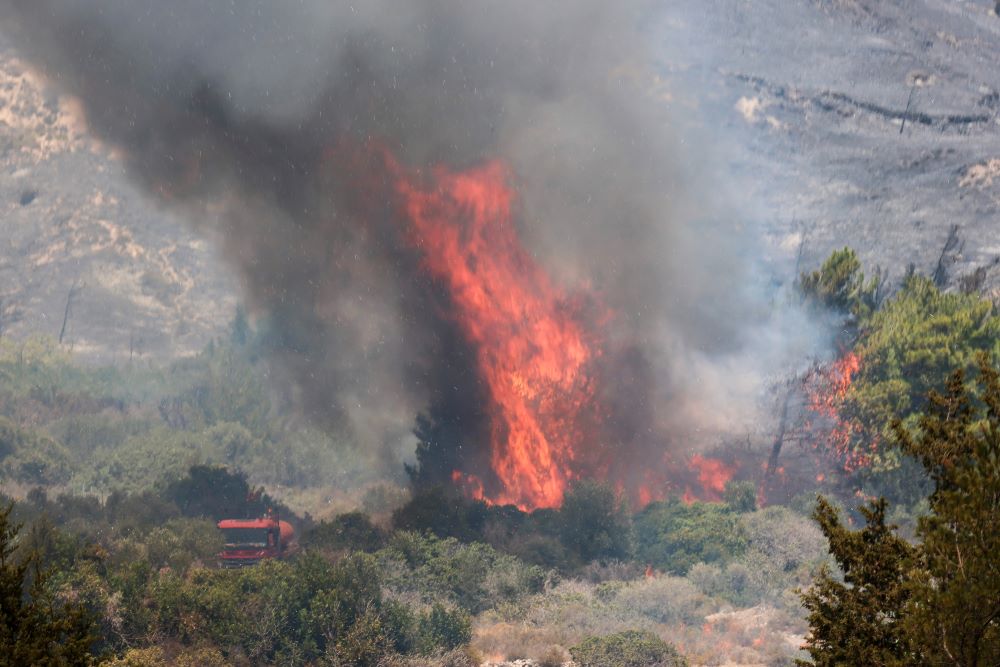 Flames rise next to a firefighting truck as a wildfire burns near the village of Vati, on the island of Rhodes, Greece, July 25, 2023. (OSV News/Reuters/Nicolas Economou)