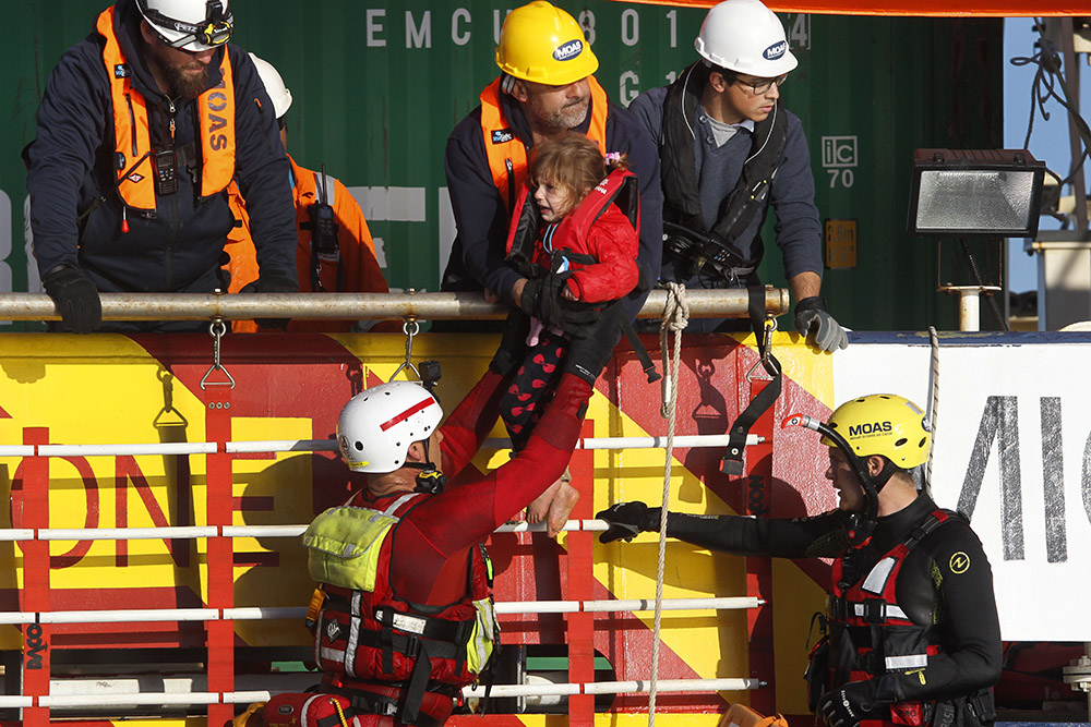 A Syrian migrant child is helped by members of MOAS, Migrant Offshore Aid Station, a Malta-based organization, to board the rescue vessel on the Aegean Sea between the eastern Greek Island of Agathonisi and the Turkish shores, Thursday, March 3, 2016. (AP/Lefteris Pitarakis)