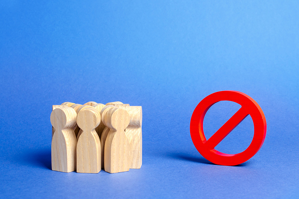 A group of wooden figures representing people stand to the side of a large red "no" symbol (Dreamstime/Andrii Yalanskyi)