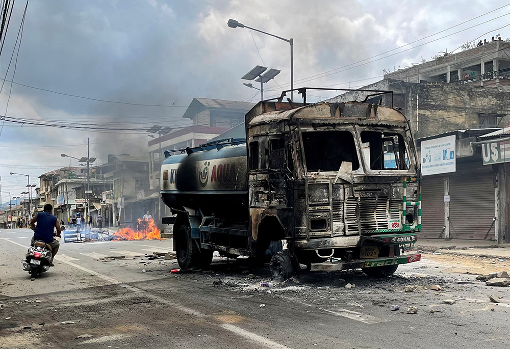 A man rides a scooter past a destroyed water tanker in Manipur, India, May 4, that was set on fire during a protest by tribal groups. The ongoing clash, which began May 3, is between the majority Meitei community (who are mostly Hindu) and Kukis, one of the tribes in the state, most of them Christian). (OSV News/Reuters)