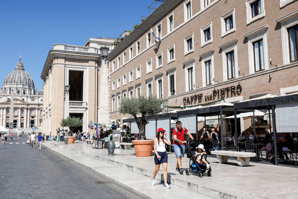 Tourists walk down a commercial street where St. Peter's Basilica is visible at the end