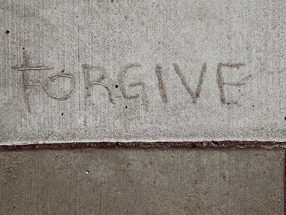 The word "FORGIVE" drawn into concrete (Unsplash/Christopher Stites)