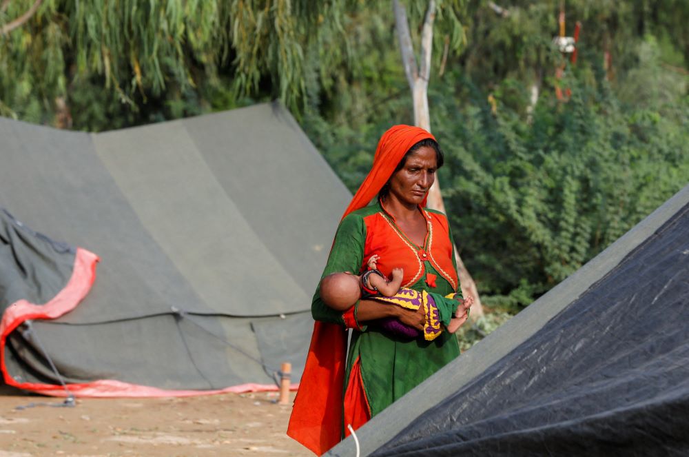 A woman who became displaced following rains and floods during the monsoon season holds her baby while standing outside her tent in Sehwan, Pakistan, Sept. 13, 2022. (OSV News/Reuters/Akhtar Soomro)