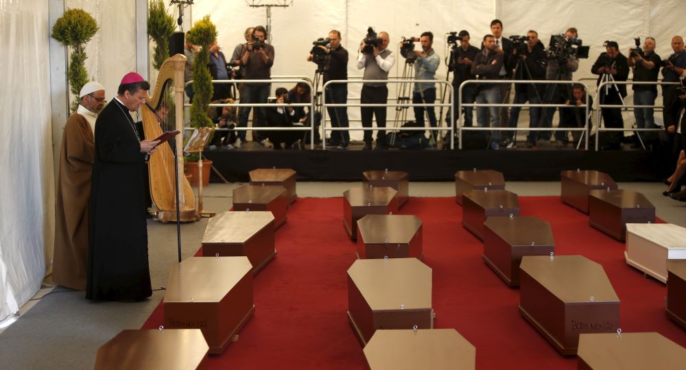 Cardinal Grech stands near rows of coffins as he prays at a memorial for migrants. 