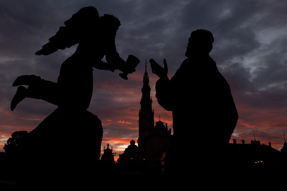 An angel and another figure are silouhetted in black against a blue and pink sunset.