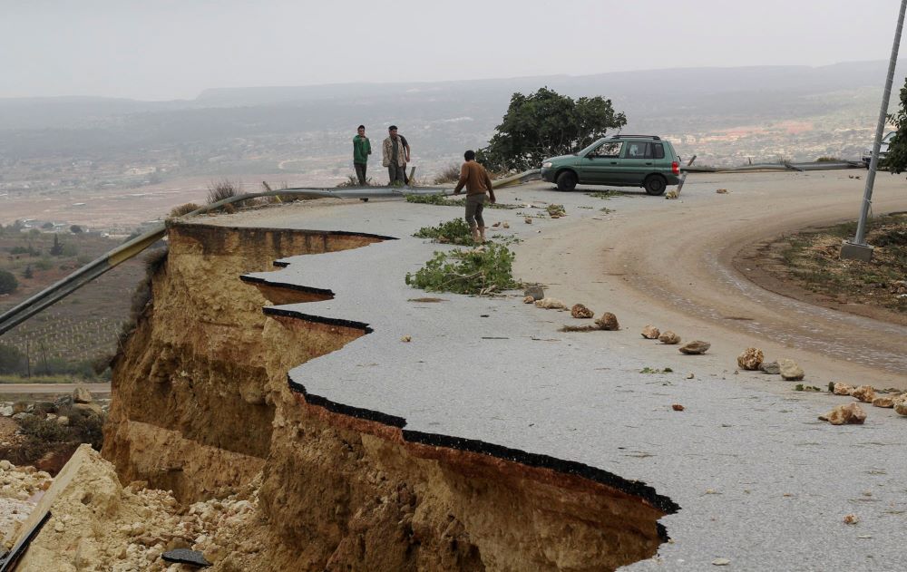 People stand in a damaged road as a powerful storm and heavy rainfall flooded hit Shahhat city, Libya