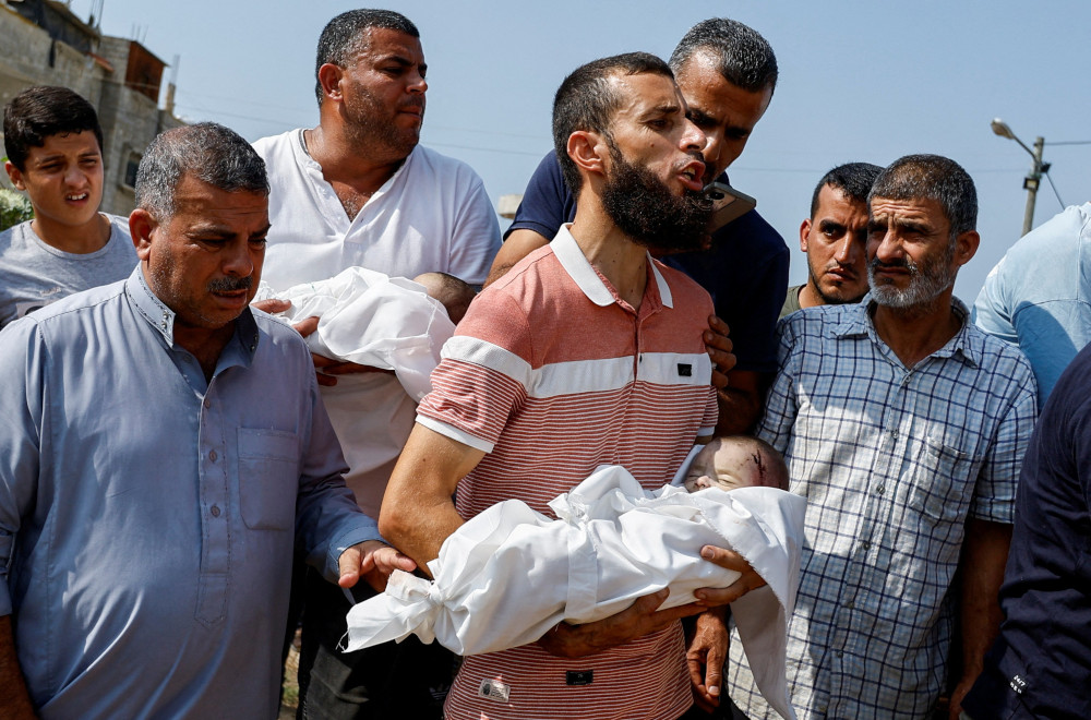 A group of brown men look sorrowful. Two carry infants wrapped in white. Blood is visible on one baby's head.