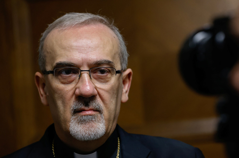 A light-skinned man with a white beard wearing glasses looks at the camera