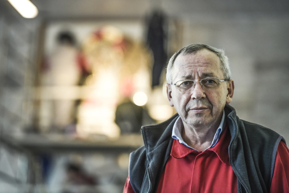 An older white man wearing glasses, a vest, and a collared shirt looks at the camera