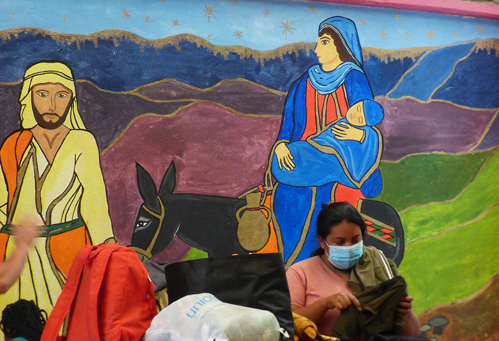 Una mujer recoge sus pertenencias frente a un mural de José y María en el refugio para migrantes Cafemin, en Ciudad de México, el 24 de agosto. La Hna. María Soledad Morales Ríos, una de las hermanas Josefinas cuya congregación gestiona el refugio, afirmó que su carisma consiste en cuidar de los pobres, incluidos los migrantes, del mismo modo que José y María cuidaron de Jesús. (Foto: GSR/Rhina Guidos)