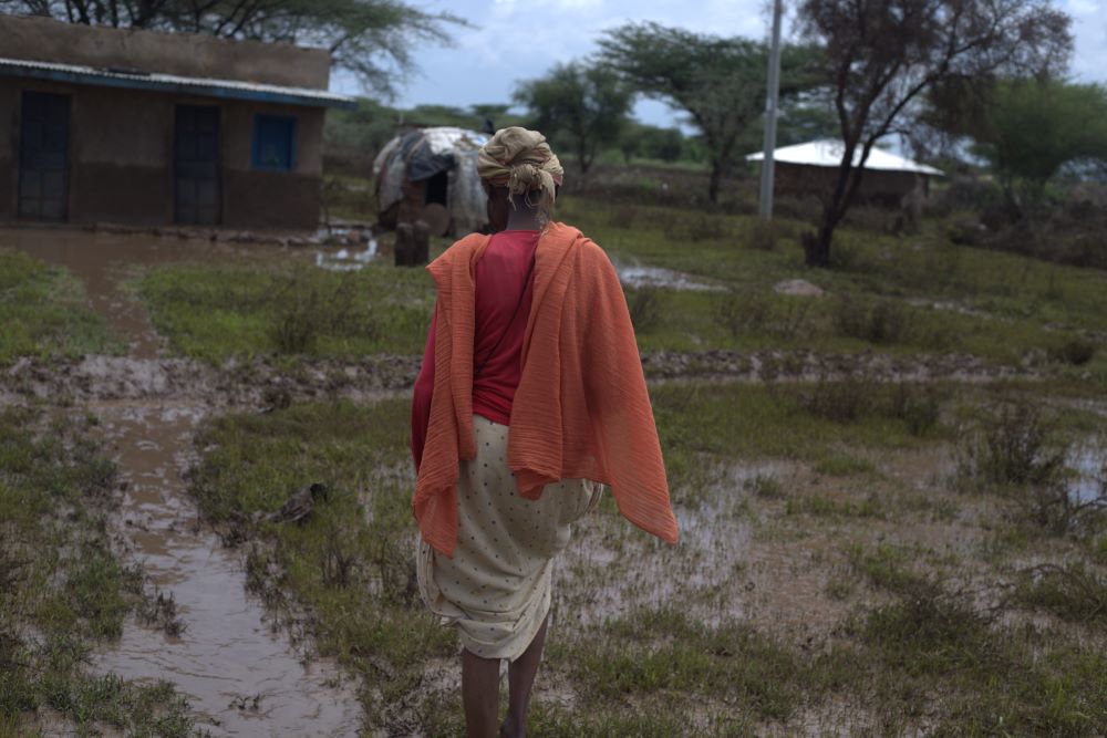 A woman walks through puddles toward a building. 