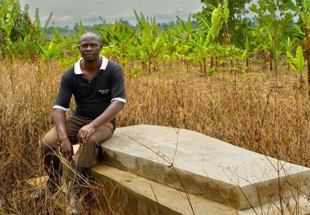 Man sits on a grave that is covered with a cement or stone box.