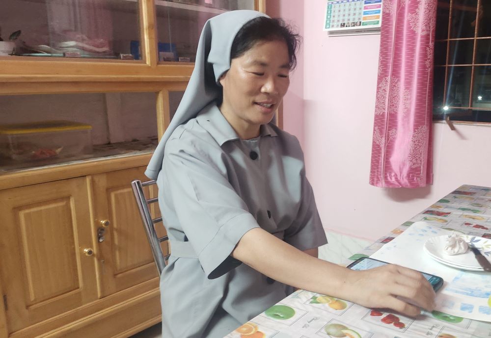 Salesian Sr. Tresa Karottukunnel sits at a table, looking at a computer tablet.